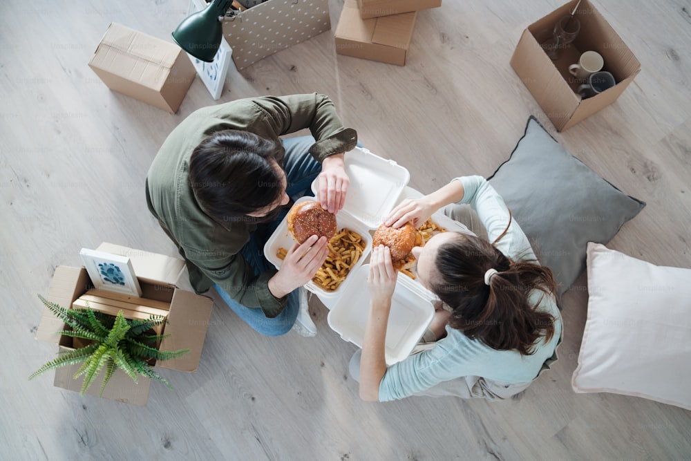 Vista superior de una pareja joven con hamburguesas y cajas que se mueven en un nuevo piso, un nuevo hogar y un concepto de reubicación.