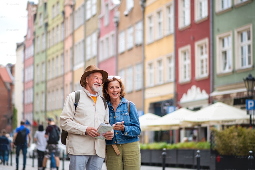 A portrait of happy senior couple tourists using map and smartphone outdoors in town street