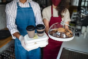 Unrecognizable young waiters preparing a take away order, looking at camera. Coronavirus concept.