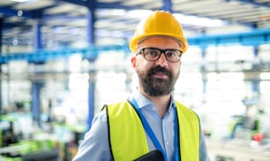 Vue de face d’un technicien ou d’un ingénieur avec un casque de sécurité debout dans une usine industrielle, regardant la caméra.