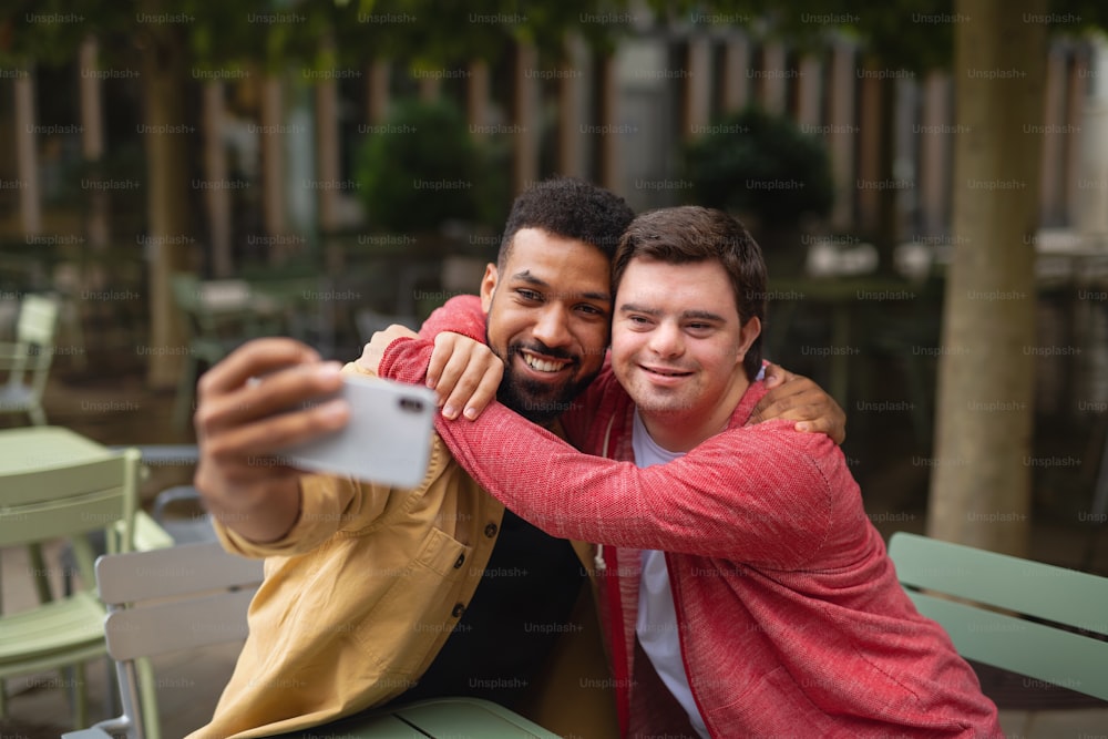 Un giovane con la sindrome di Down e il suo amico mentore seduti e scattano selfie all'aperto in un caffè