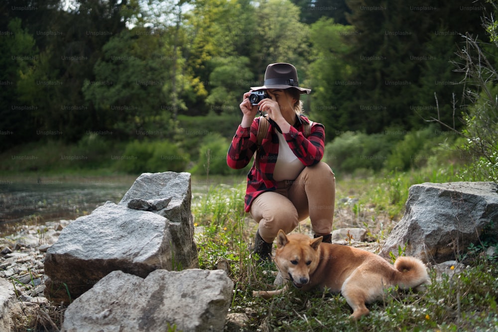 Vista frontal de una mujer joven con un perro en un paseo al aire libre en la naturaleza de verano, tomando fotografías.