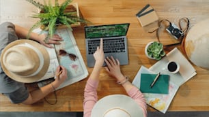 Vista superior de una pareja joven irreconocible con una computadora portátil y mapas que planifican vacaciones de viaje, concepto de viaje de escritorio.