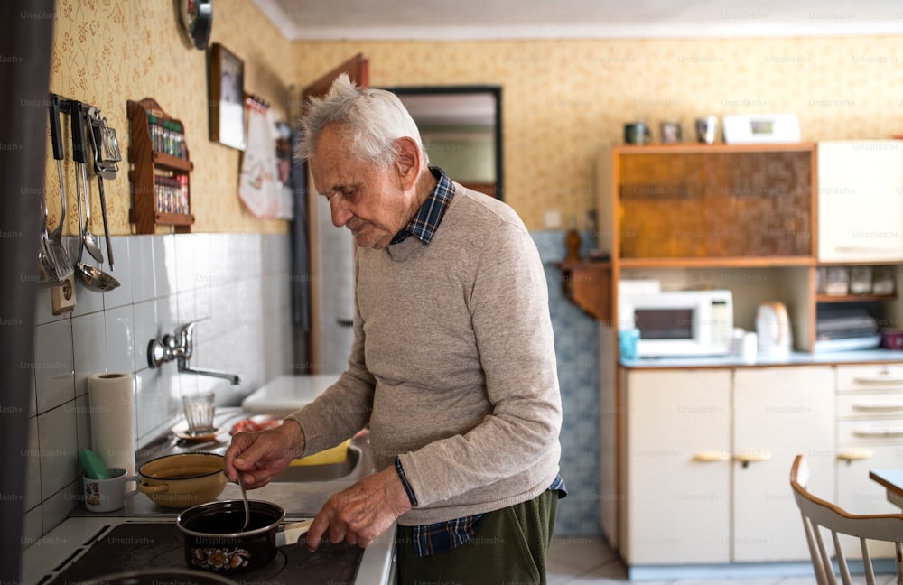 A portrait of elderly man cooking on stove indoors at home, stirring.