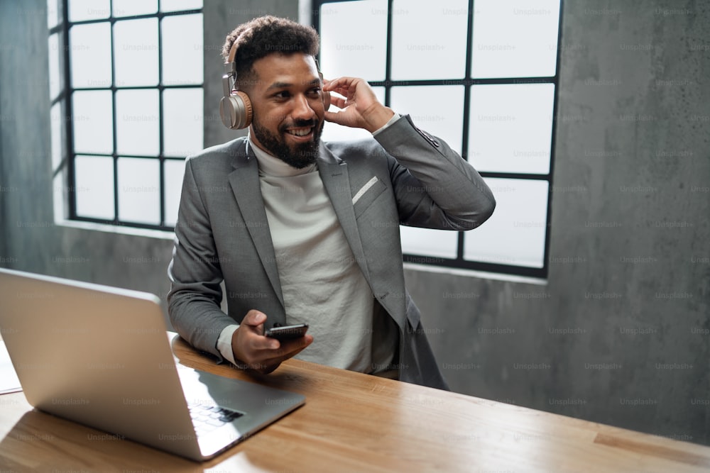 Giovane uomo d'affari afroamericano felice con uno smartphone che lavora su un computer portatile all'interno dell'ufficio