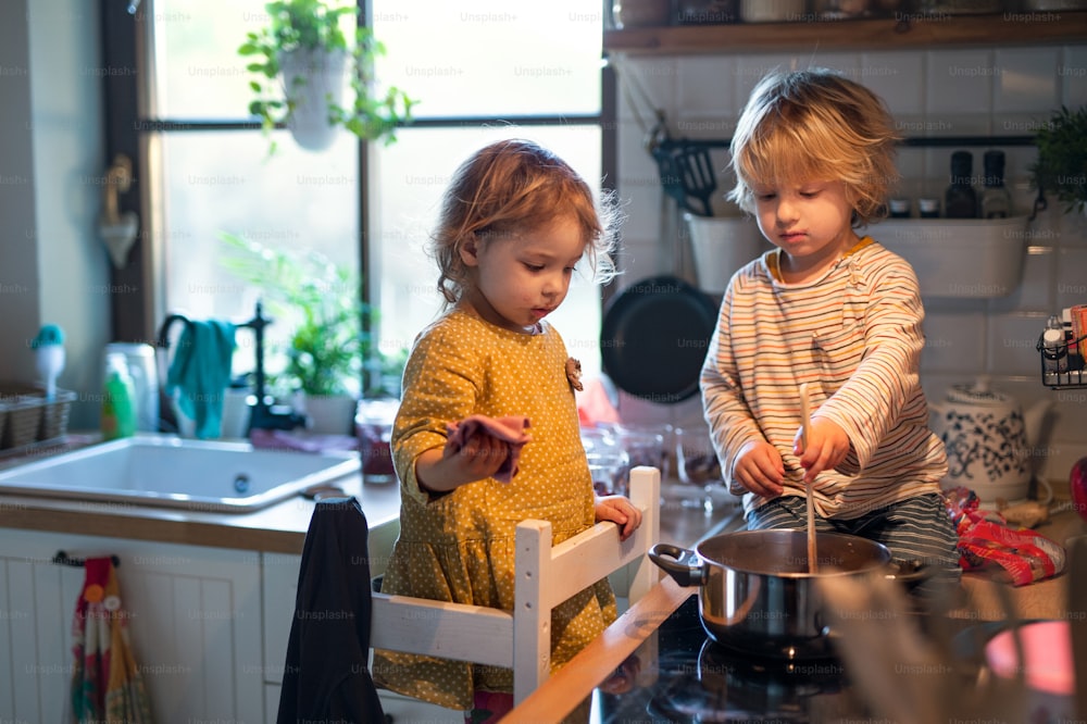 幸せな小さな男の子と女の子は、自宅のキッチンで屋内で料理を手伝っています。