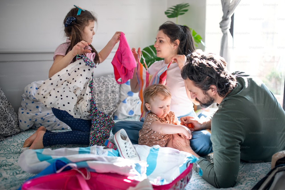 Portrait of family with two small daughters packing for holiday on bed at home.