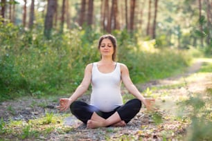 Front view portrait of happy pregnant woman outdoors in nature, doing yoga exercise.