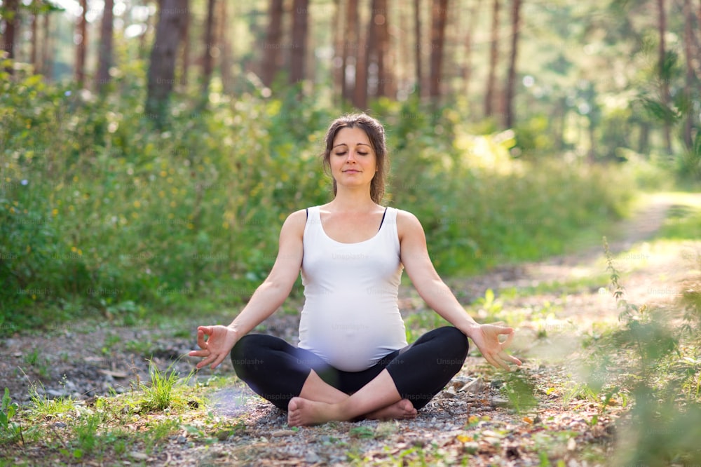 Front view portrait of happy pregnant woman outdoors in nature, doing yoga exercise.