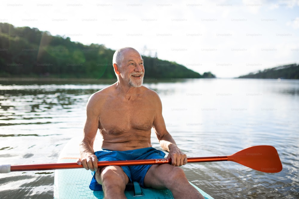 Vista frontale dell'uomo anziano seduto sul paddleboard sul lago in estate. Copia spazio.