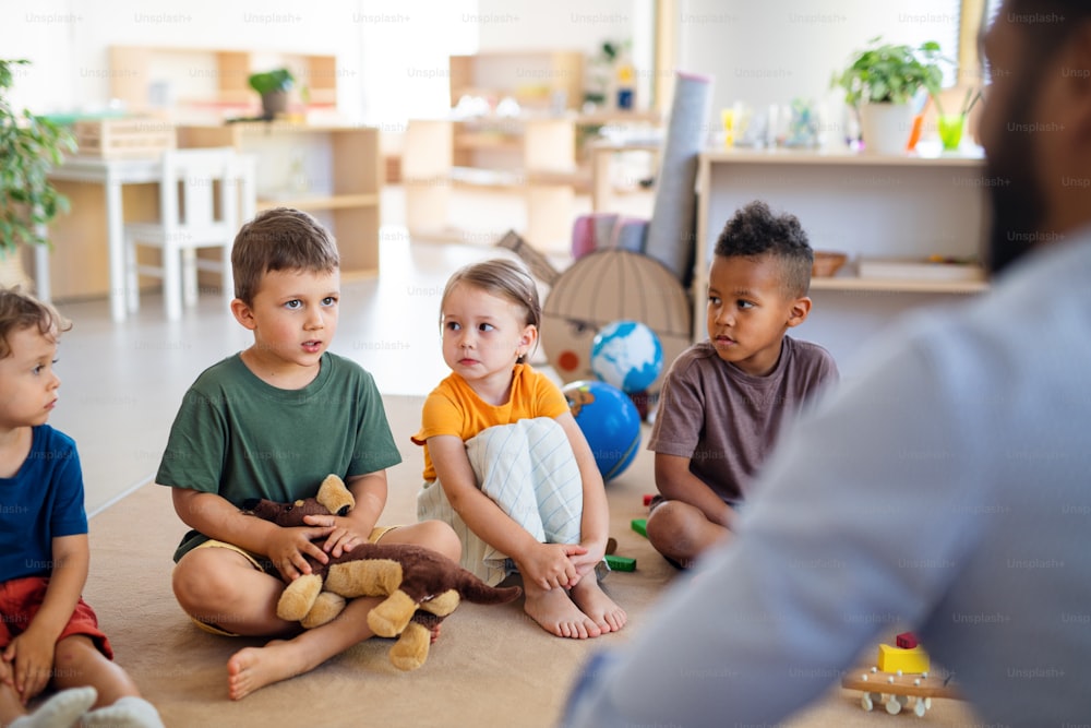 Un grupo de pequeños niños de guardería sentados en el suelo en el interior del aula.