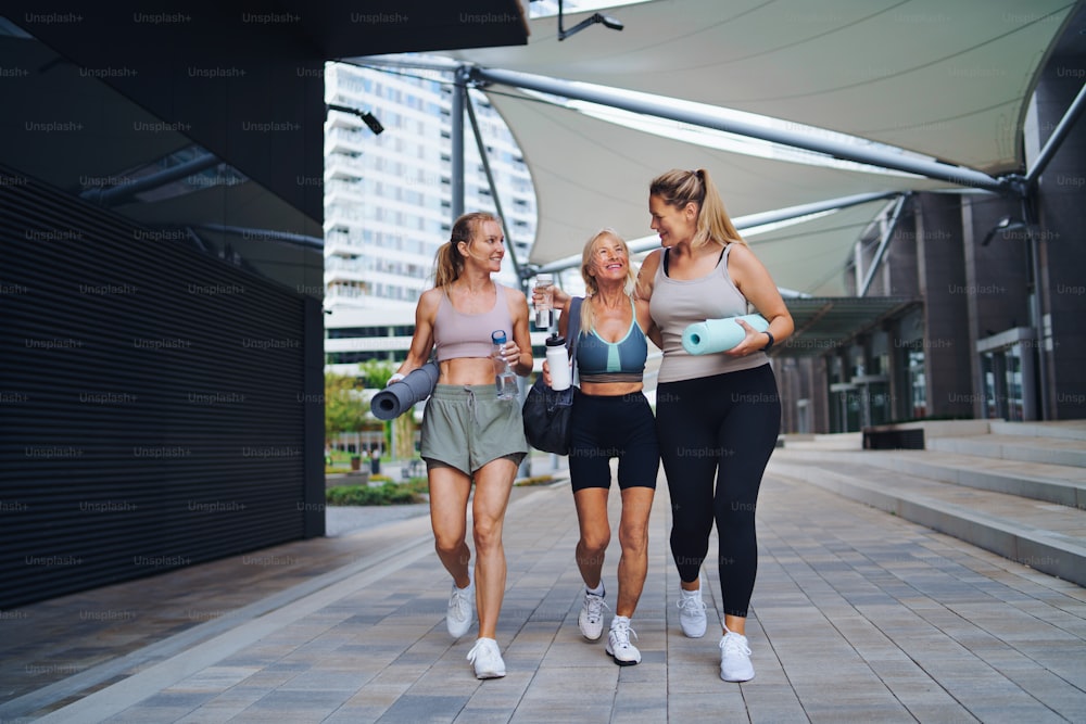 Un grupo de mujeres jóvenes y ancianas que caminan después de hacer ejercicio al aire libre en la ciudad, hablando.