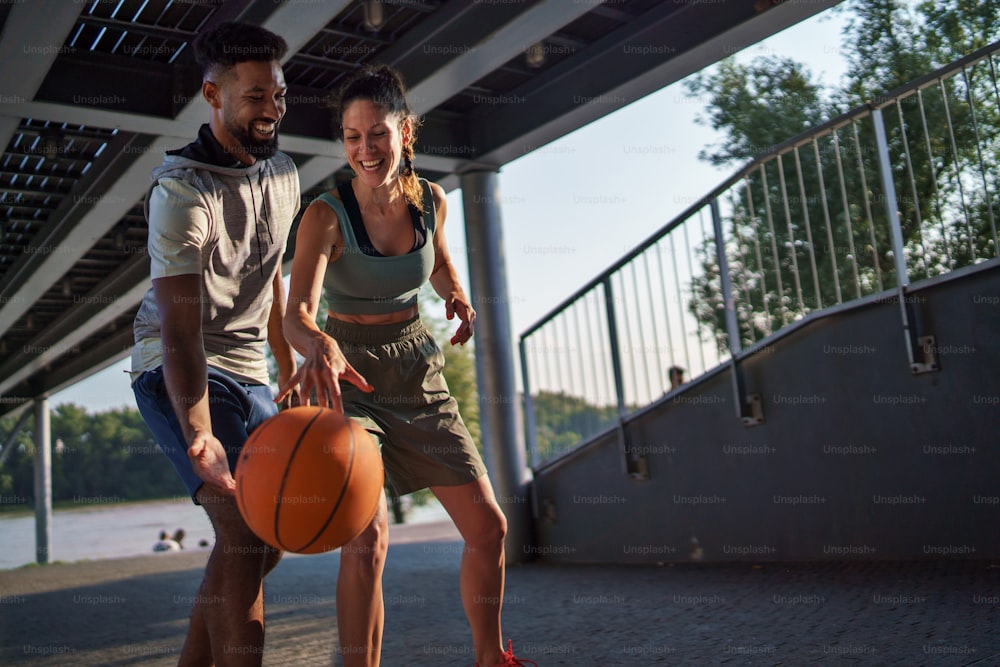 A man and woman friends playing basketball outdoors in city.
