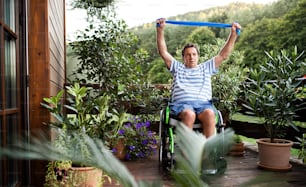 A senior man in wheelchair doing exercise on terrace.