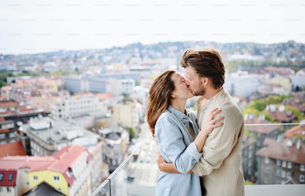 Una feliz pareja joven enamorada de pie al aire libre en el balcón de su casa, besándose.
