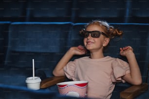 Happy small girl with 3d glasses and popcorn in the cinema, watching film.