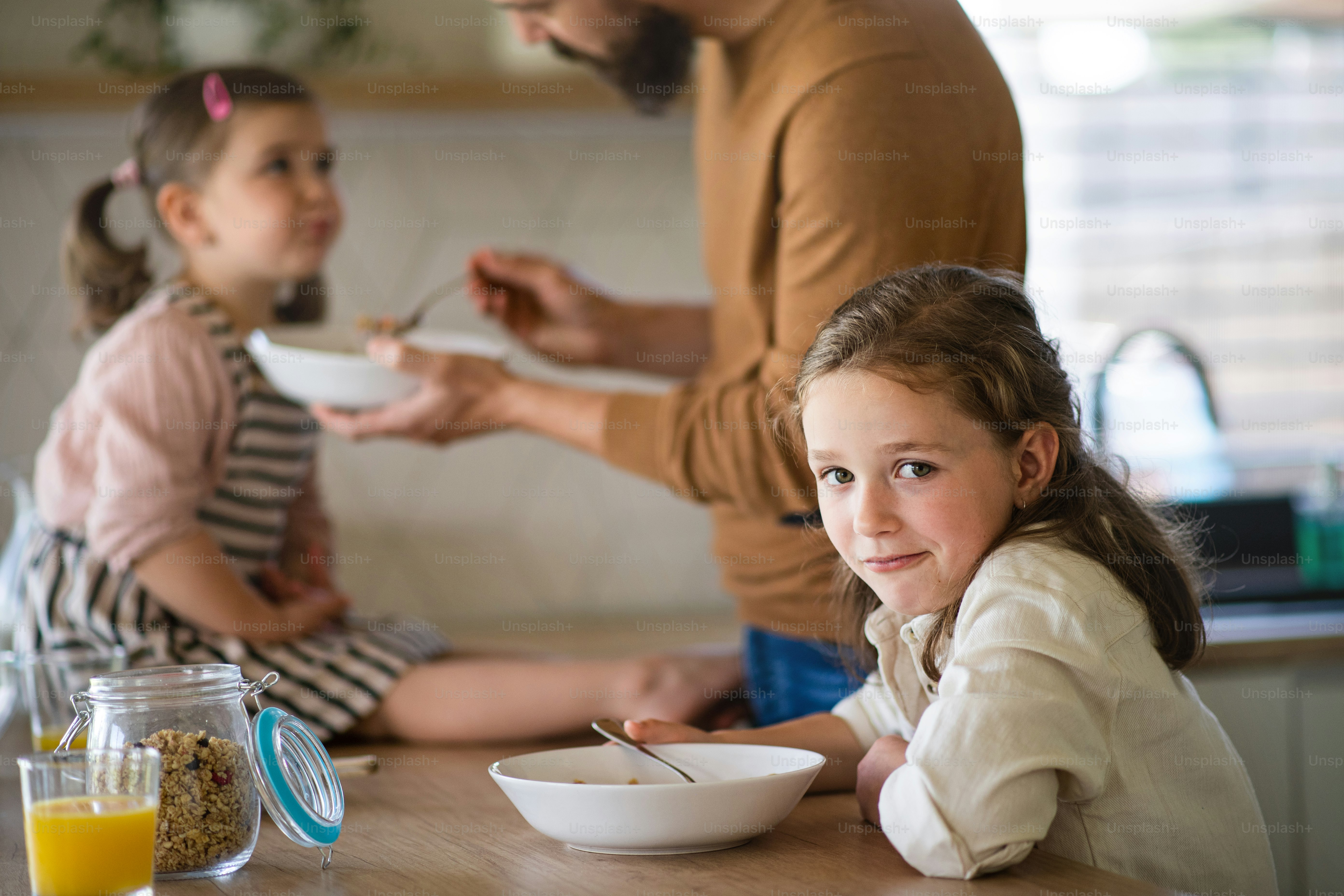 A father with daughters indoors at home, eating breakfast in kitchen