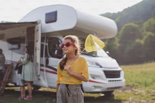 A happy small girl with sunglasses standing outdoors by caravan car, family holiday trip.