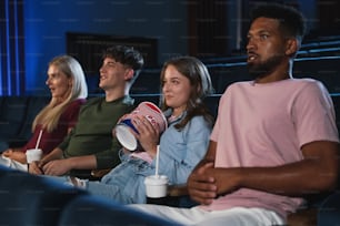 Jovens com pipoca e bebidas no cinema, assistindo a um filme de suspense.