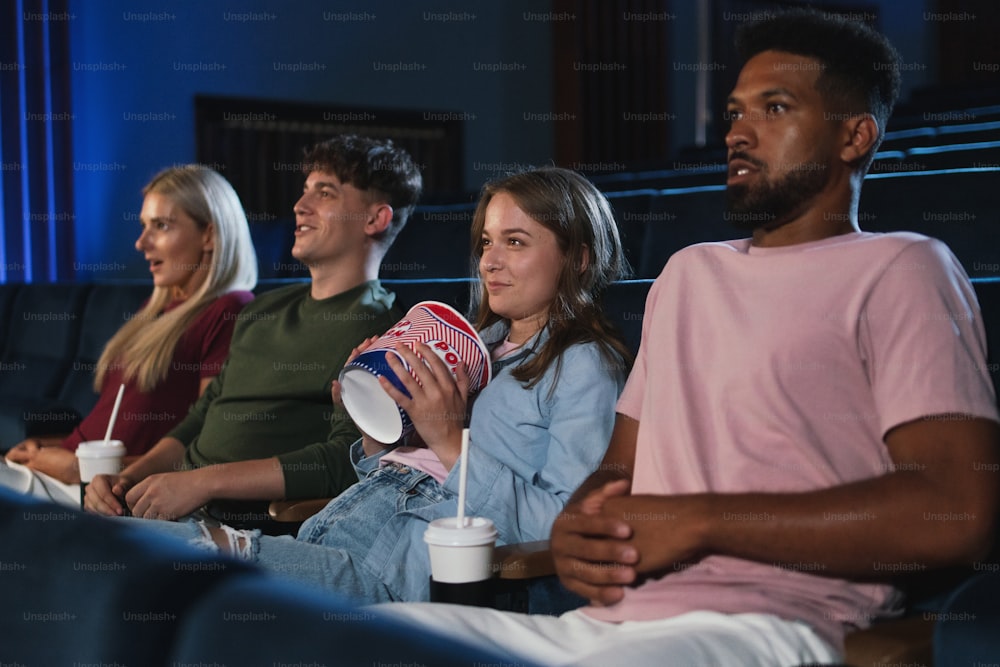 Jóvenes con palomitas de maíz y bebidas en el cine, viendo una película de suspenso.