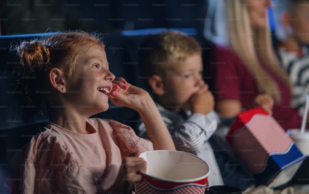 A small girl with family sitting and watching film in the cinema, eating popcorn