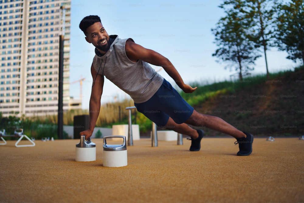 Young man doing workout exercise outdoors in city, push up on one hand.