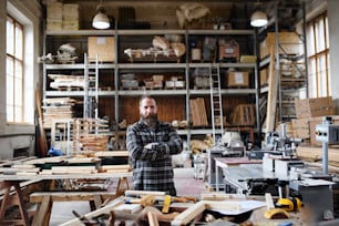 Carpintero masculino maduro feliz de pie en el taller de carpintería, mirando a la cámara. Concepto de pequeña empresa.