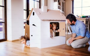Due bambini felici con il padre che gioca con la casa di carta all'interno della casa.