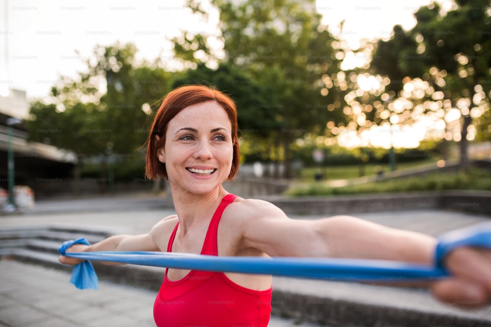A portrait of young woman doing exercise outdoors in city with elastic bands.