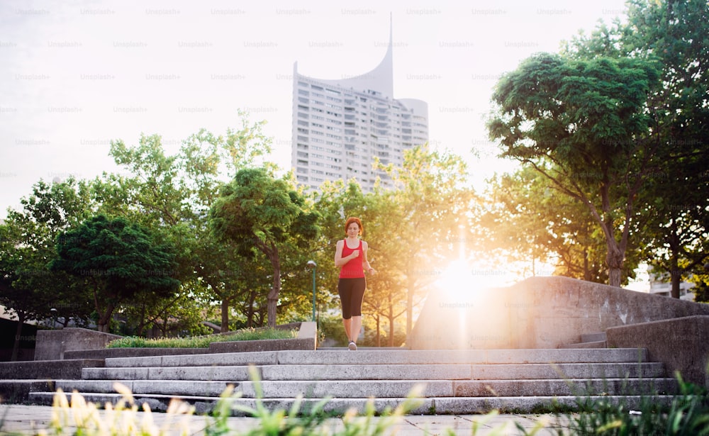 Young woman runner jogging outdoors in city at sunrise early in the morning.