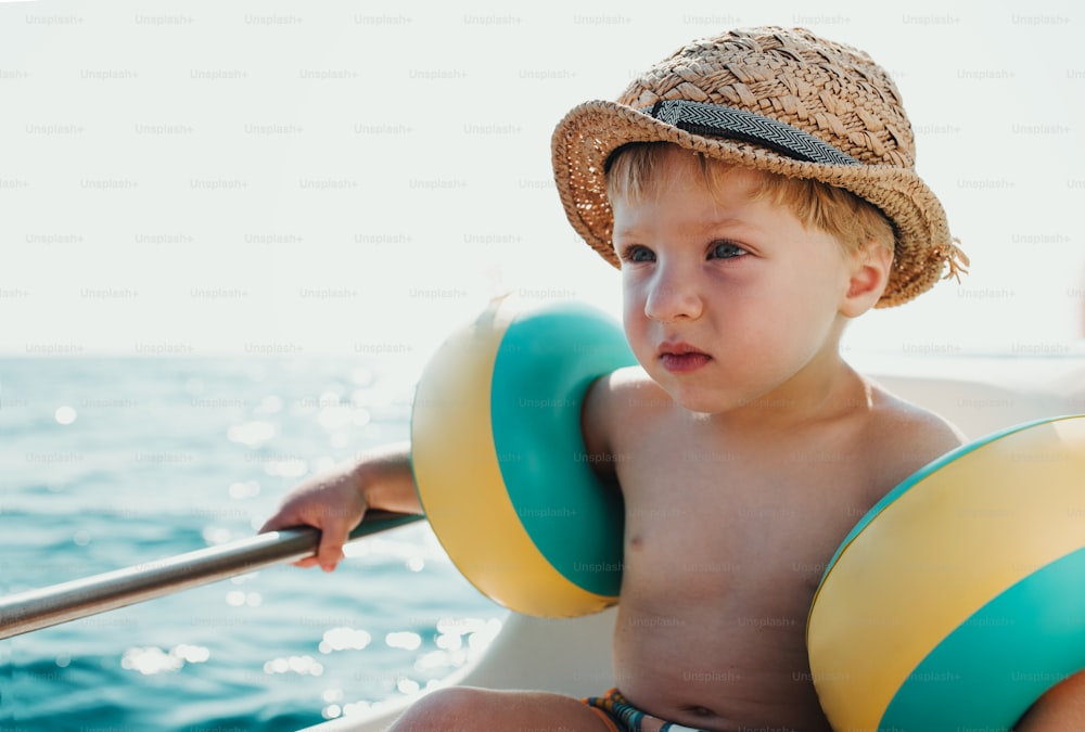 A small boy with armbands sitting on boat on summer holiday, holding a railing.