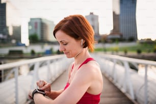 A young woman with smartwatch on bridge outdoors in city, resting after exercise.