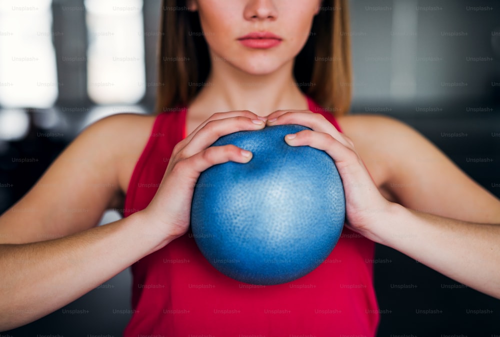 A midsection of beautiful young girl or woman doing exercise with a ball in a gym.