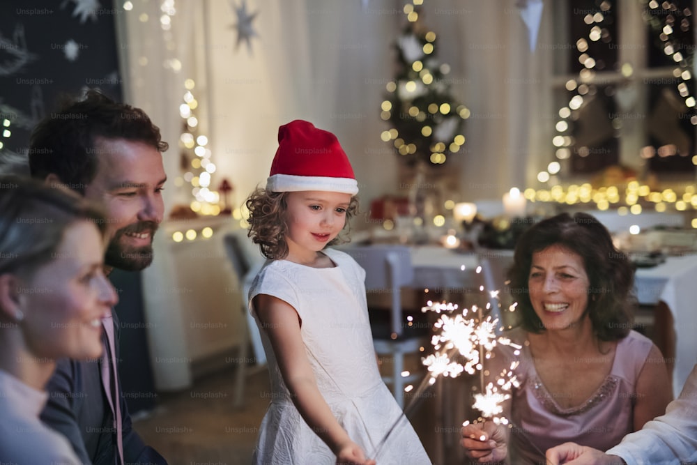 Small girl with parents and grandparents indoors celebrating Christmas, holding sparklers.