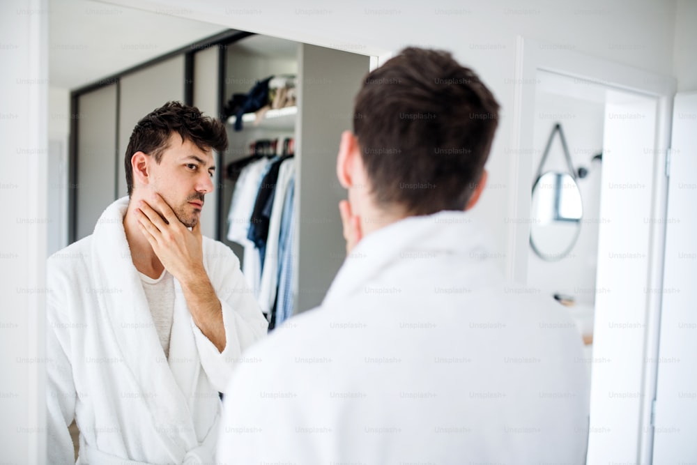 A young man looking in mirror in bedroom in the morning, daily routine.
