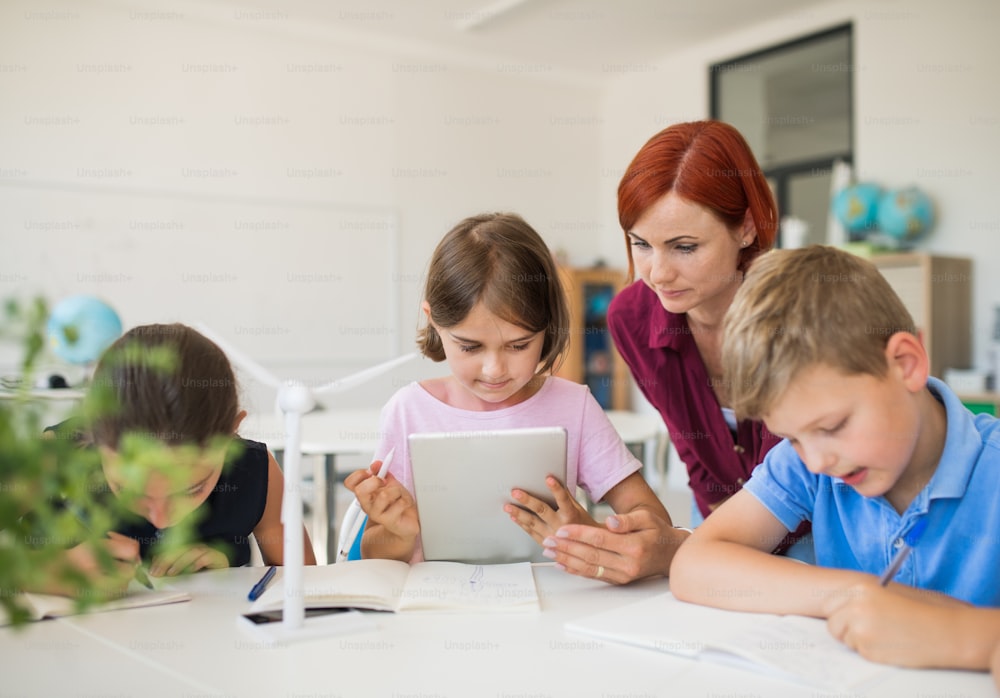 태블릿을 사용하여 교실에서 서클에 앉아 있는 교사와 함께 작은 학교 아이들.