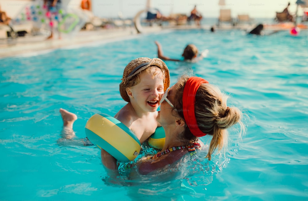 Um menino pequeno e feliz com braçadeiras e sua mãe nadando na água nas férias de verão.