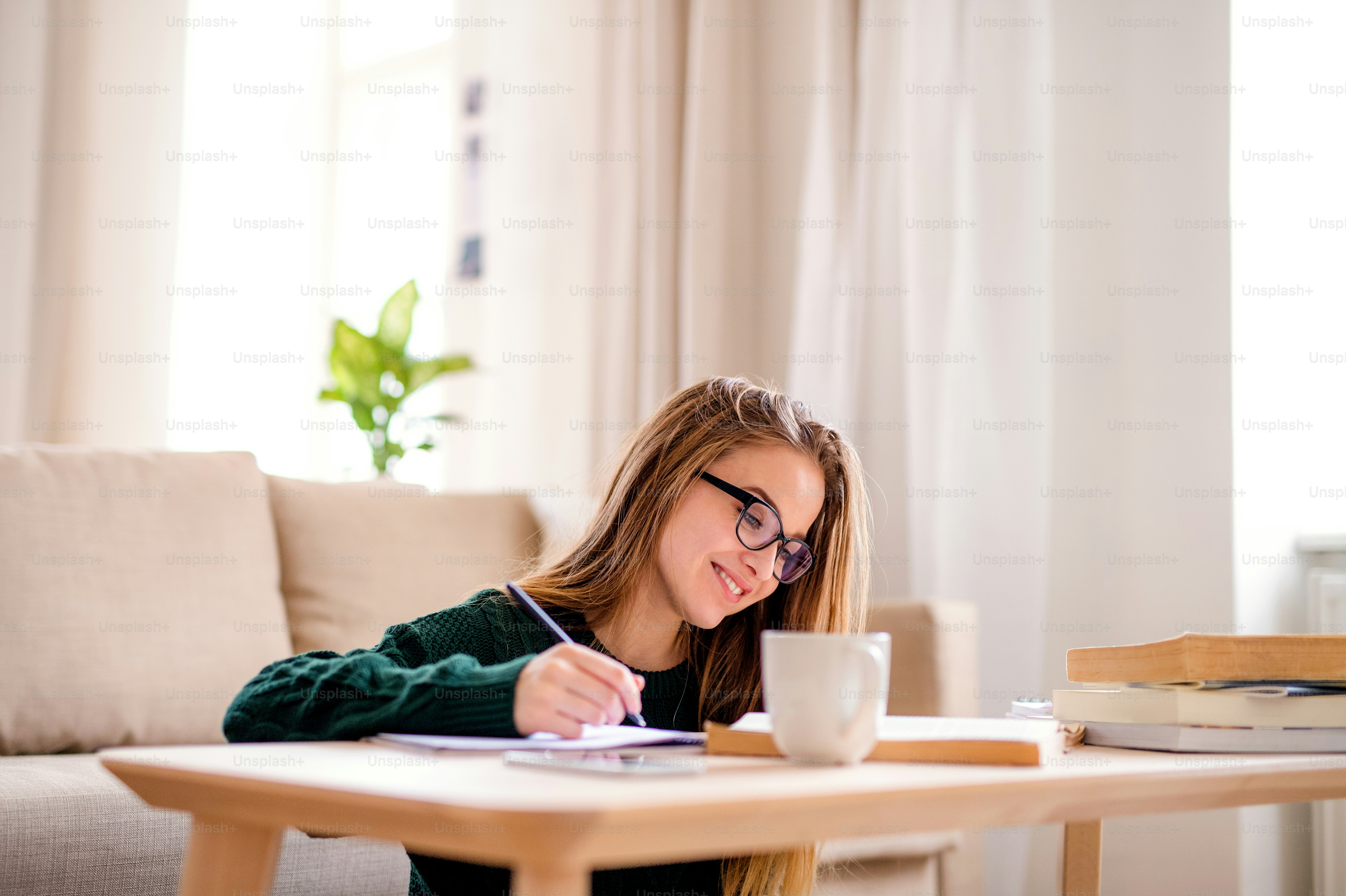 Eine junge, unglückliche und traurige Studentin, die zu Hause am Tisch sitzt und studiert.
