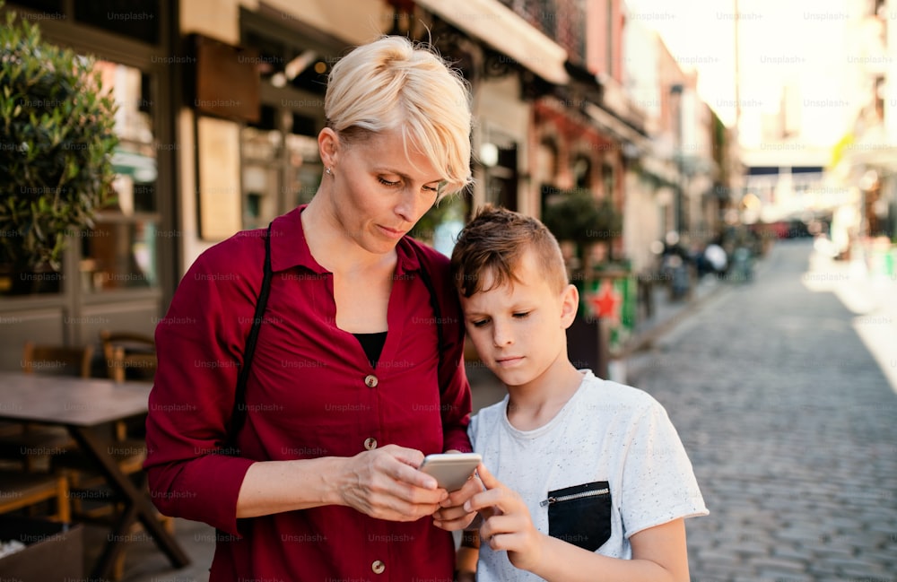Mother with son standing outdoors in Mediterranean town, looking at map on smartphone.