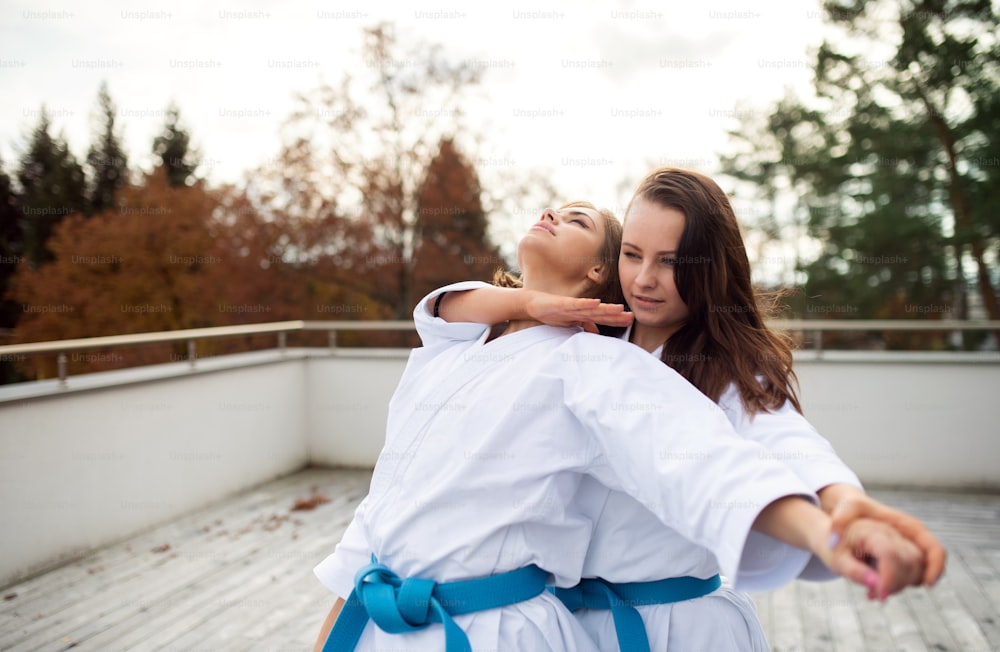 Two young women practising karate outdoors on terrace.