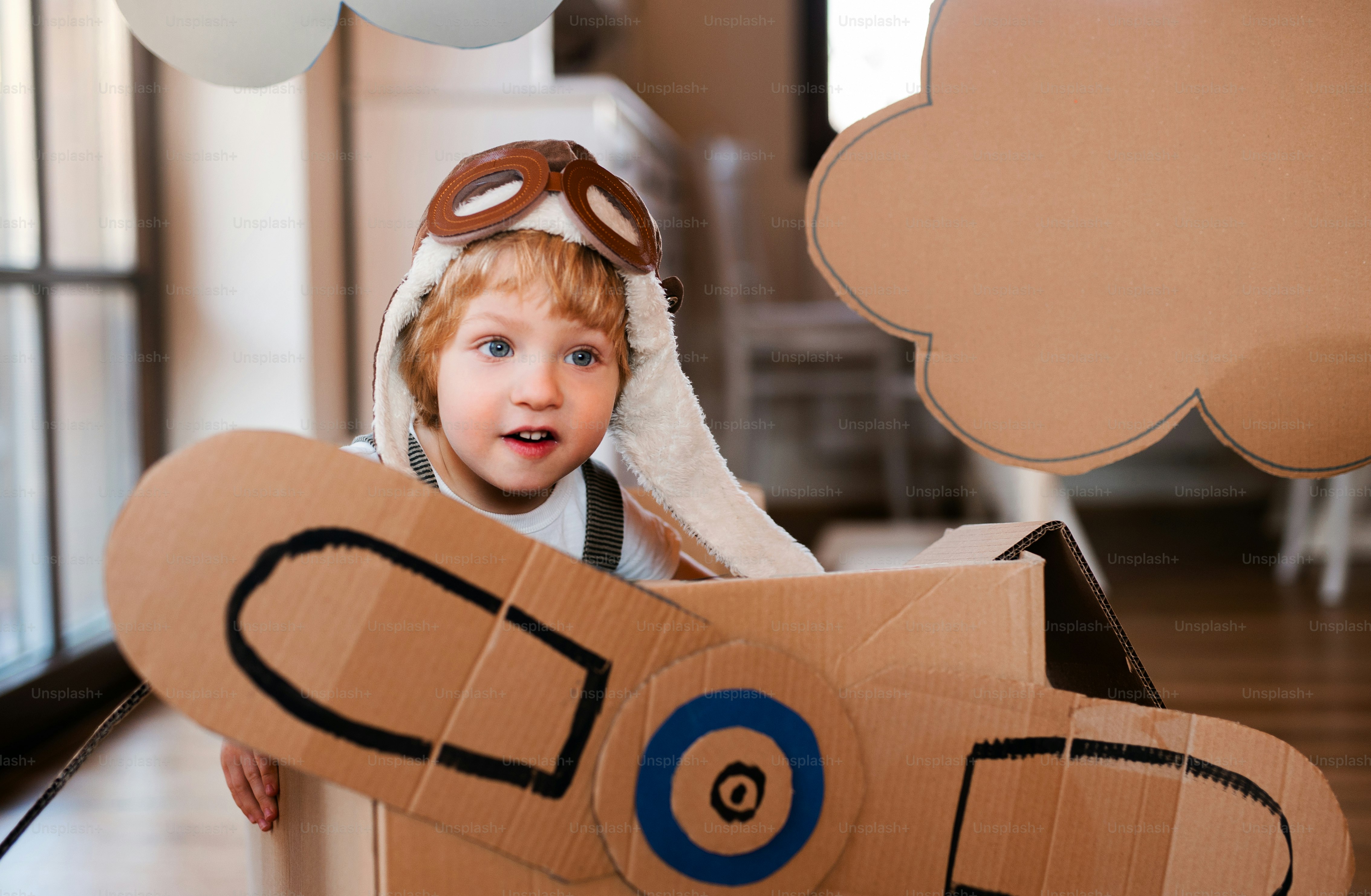 A happy toddler boy with carton plane playing indoors at home, flying concept.