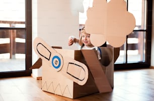 A happy toddler boy with carton plane playing indoors at home, flying concept.