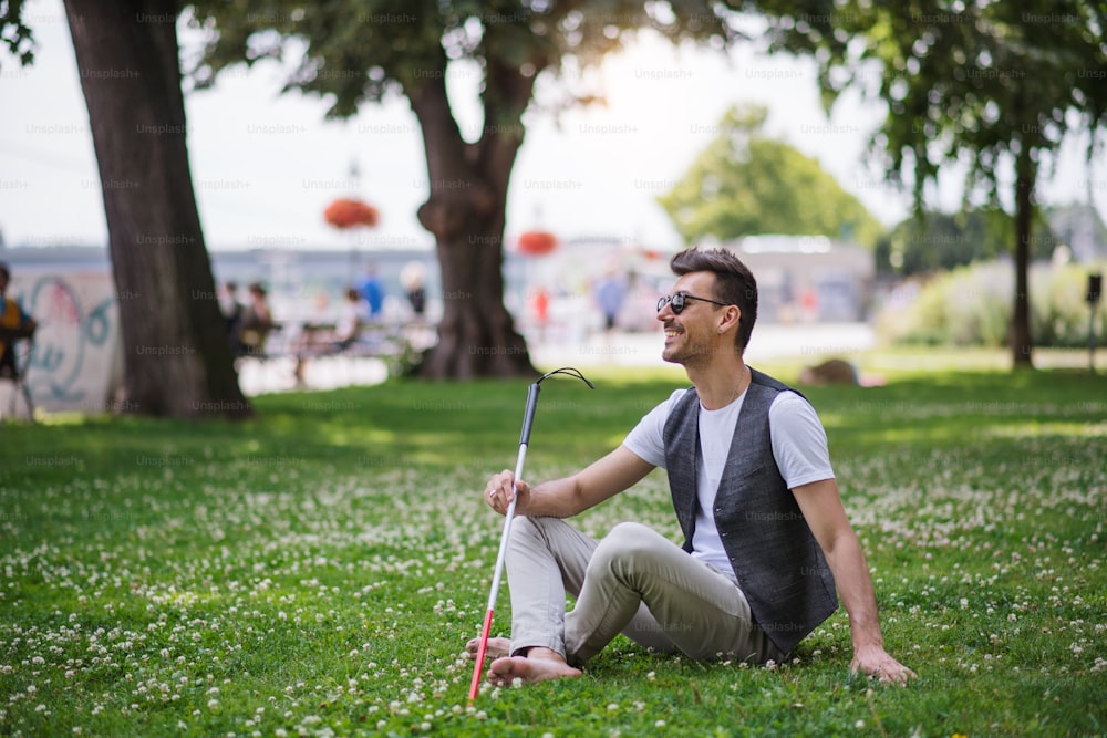 흰 지팡이와 안내견을 가진 젊은 장님이 도시의 공원에 앉아 쉬고 있다.