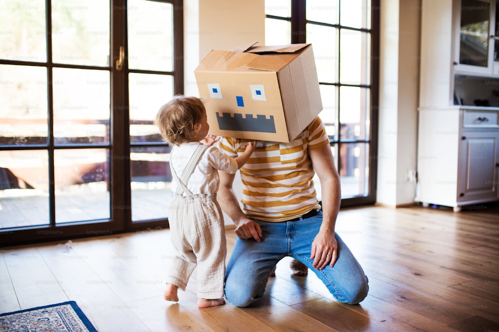 Una niña feliz con un padre y un monstruo de cartón jugando en el interior de la casa.