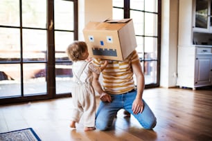 Una niña feliz con un padre y un monstruo de cartón jugando en el interior de la casa.