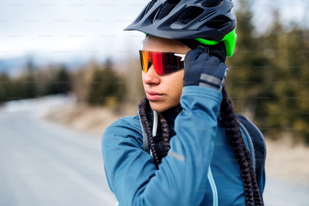 선글라스를 낀 여성 산악 자전거 타는 사람은 겨울에 야외 도로에 서 있습니다.