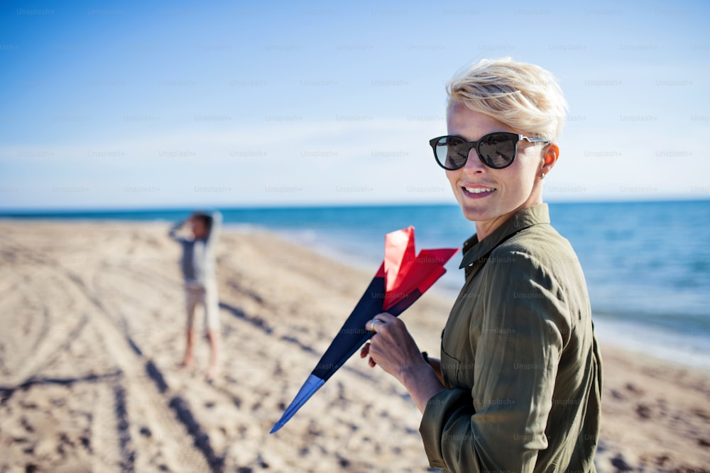 Mother with unrecognizable son standing outdoors on beach, playing with plane.