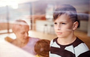 A portrait of small boy with family at home, looking out of window. Shot through glass.