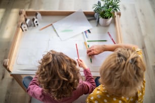 A top view of unrecognizable small girl with mother indoors at home, drawing pictures.