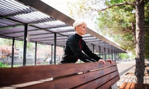 A portrait of young sportswoman doing exercise outdoors in park, stretching by bench.